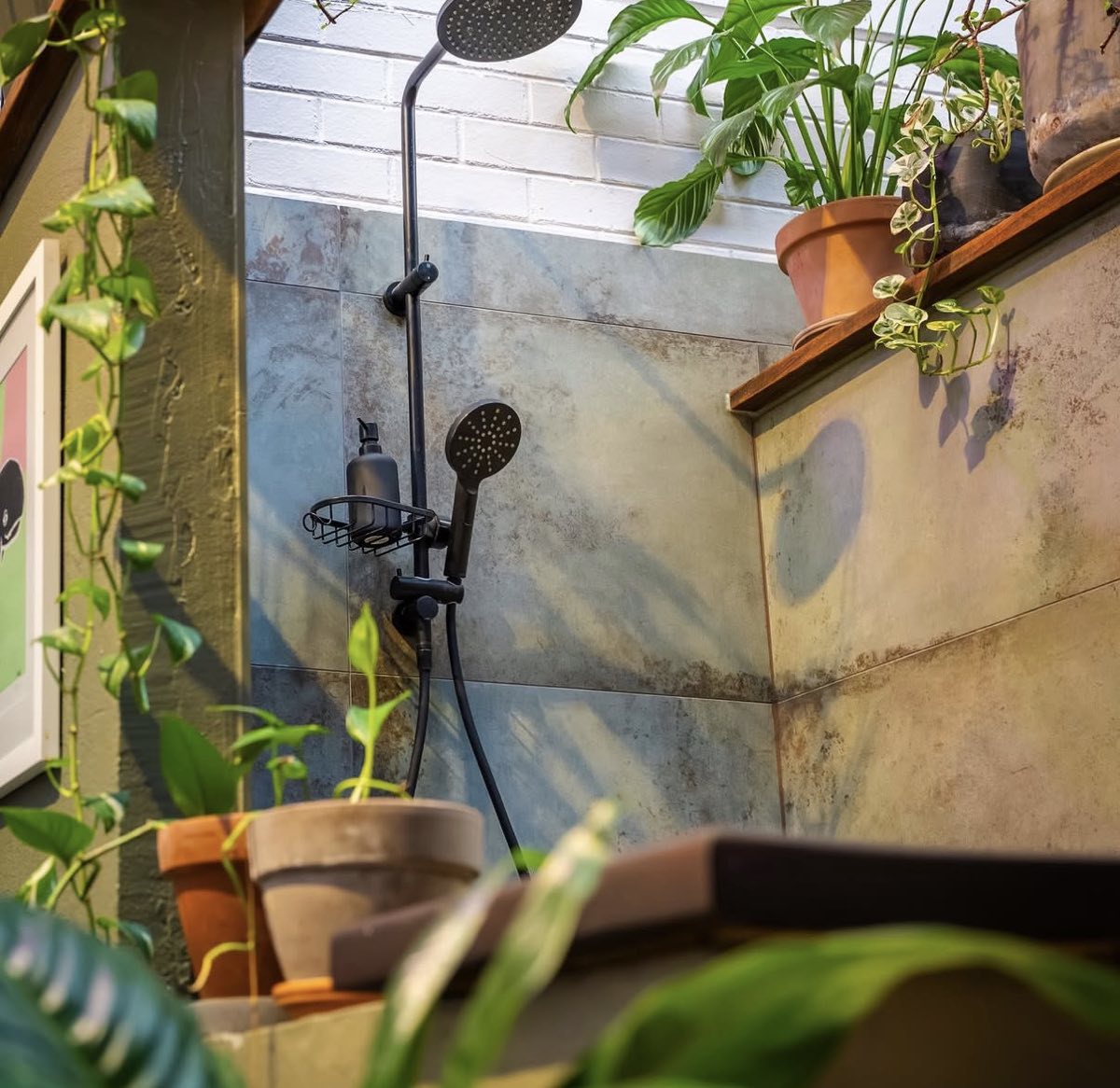 Open shower area with tiled walls and hanging plants